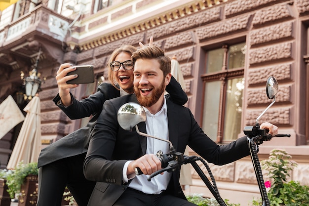 Feliz pareja gritando elegante sentado en moto moderna al aire libre