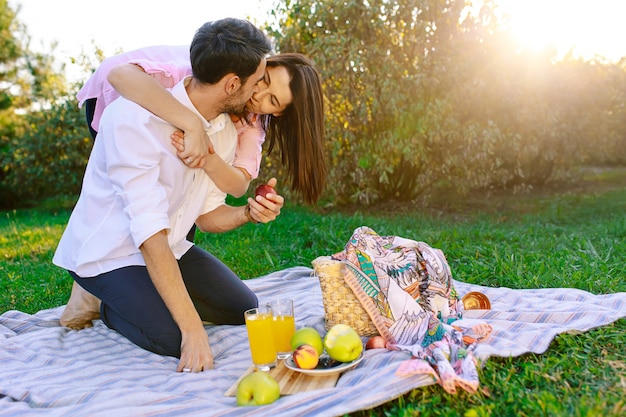 Feliz pareja haciendo un picnic en el parque en un día soleado, besándose y abrazándose