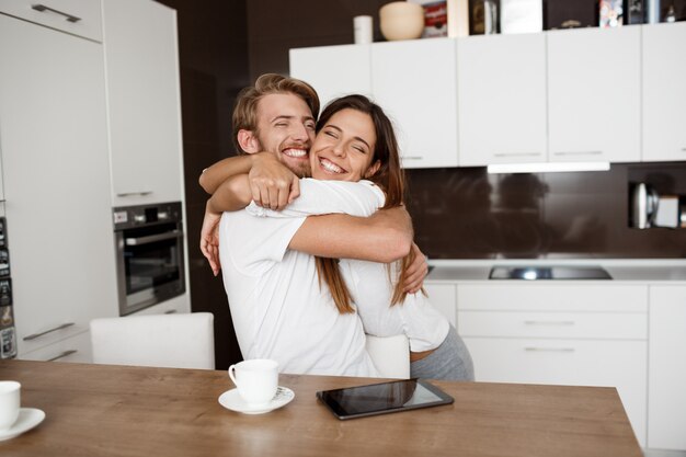 Feliz pareja hermosa abrazando sonriendo en la cocina en la mañana.