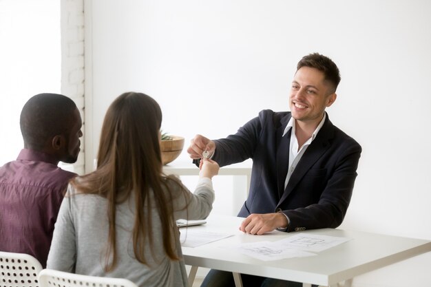 Feliz pareja interracial recibiendo las llaves de la nueva casa de la inmobiliaria