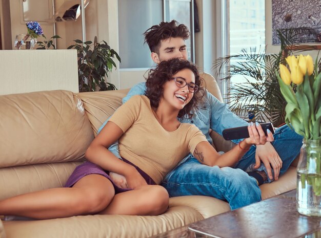 Feliz pareja joven abrazándose mientras ve la televisión en su sala de estar.