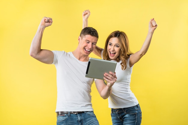 Feliz pareja joven apretando su puño mirando tableta digital riendo