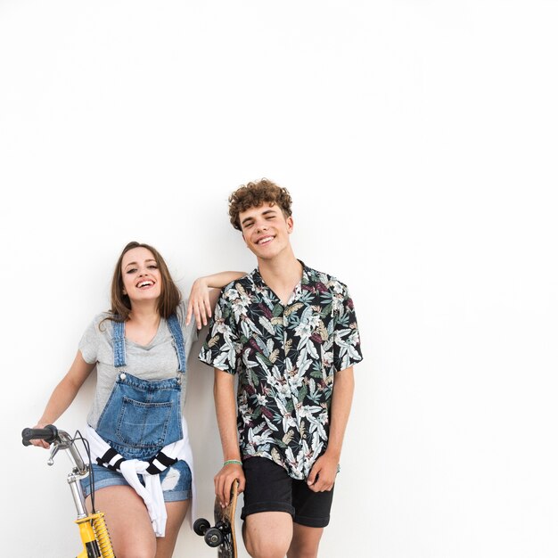 Feliz pareja joven con bicicleta y patín sobre fondo blanco