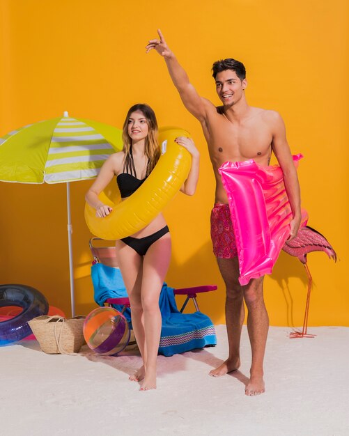 Feliz pareja joven con círculo de natación y colchón en la playa