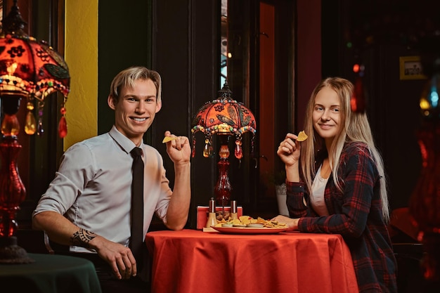 Feliz pareja joven comiendo nachos durante las citas en un restaurante mexicano.