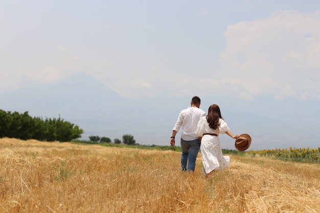Feliz pareja joven corriendo en un campo de hierba seca con cielo azul