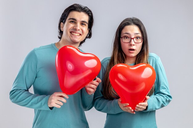 Feliz pareja joven en el día de San Valentín sosteniendo globos de corazón aislado sobre fondo blanco.