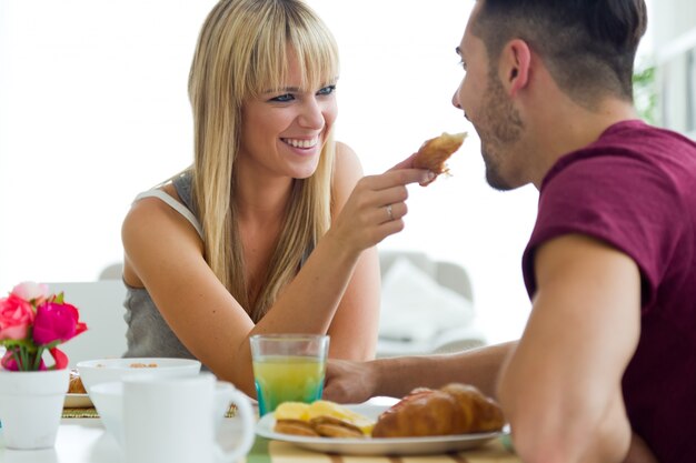 Feliz pareja joven disfrutando de desayuno en la cocina.