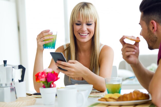 Feliz pareja joven disfrutando de desayuno en la cocina.