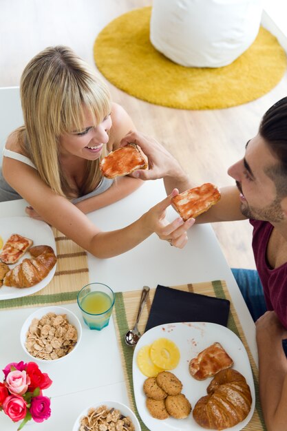 Feliz pareja joven disfrutando de desayuno en la cocina.