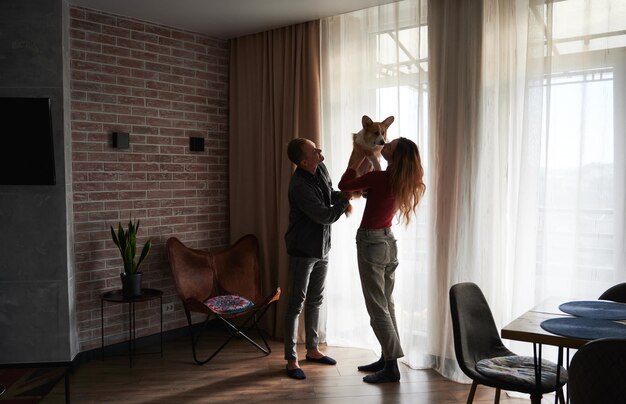 Feliz pareja joven divirtiéndose con lindo Corgi en casa