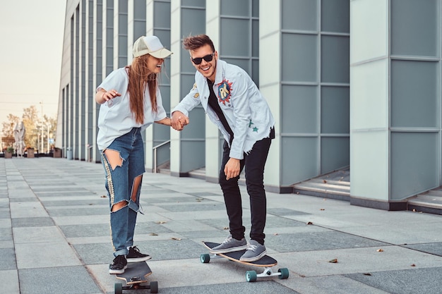 Feliz pareja joven divirtiéndose mientras conduce patinetas en la calle moderna.