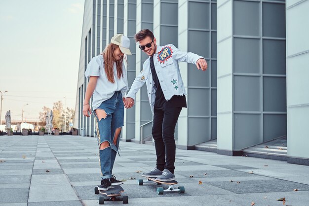 Feliz pareja joven divirtiéndose mientras conduce patinetas en la calle moderna.