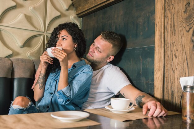 Feliz pareja joven está bebiendo café y sonriendo mientras está sentado en el café