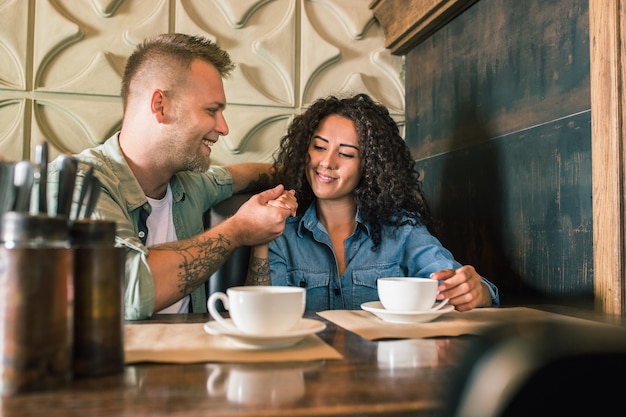 Feliz pareja joven está bebiendo café y sonriendo mientras está sentado en el café