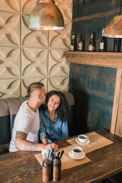 Feliz pareja joven está bebiendo café y sonriendo mientras está sentado en el café