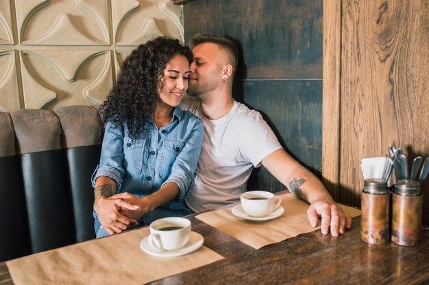 Feliz pareja joven está bebiendo café y sonriendo mientras está sentado en el café