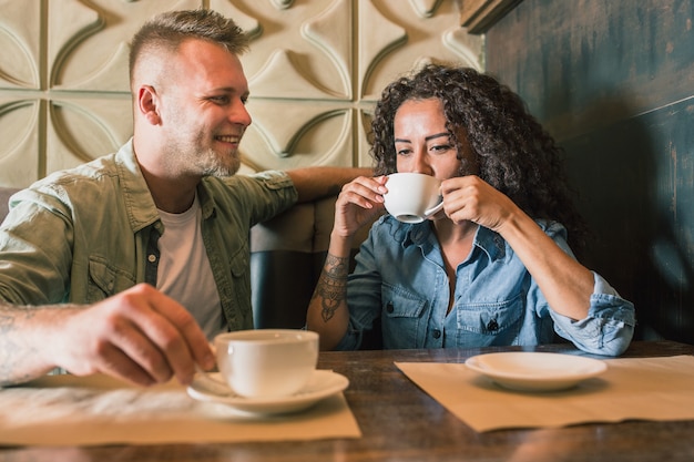 Feliz pareja joven está bebiendo café y sonriendo mientras está sentado en el café