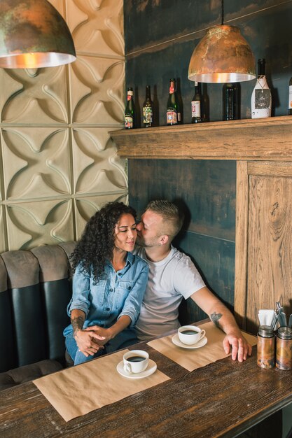 Feliz pareja joven está bebiendo café y sonriendo mientras está sentado en el café