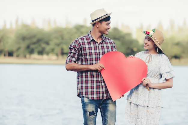 Feliz pareja joven está sosteniendo corazones de papel rojo