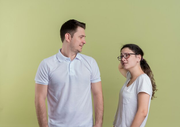 Feliz pareja joven hombre y mujer mirando el uno al otro sonriendo de pie sobre la pared de luz