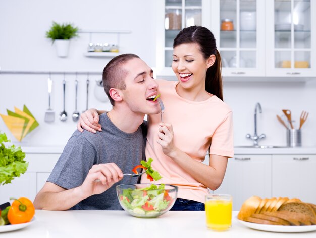 Feliz pareja joven juguetona comiendo juntos en la cocina