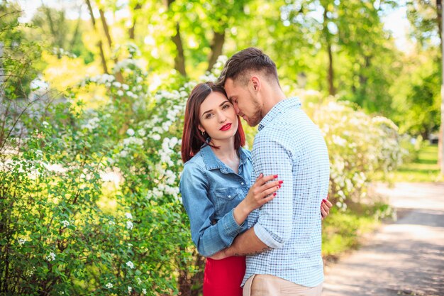 Feliz pareja joven en el parque de pie y riendo en el brillante día soleado