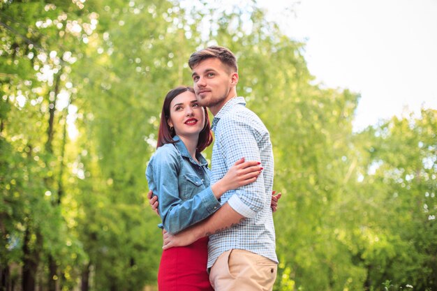 Feliz pareja joven en el parque de pie y riendo en el brillante día soleado