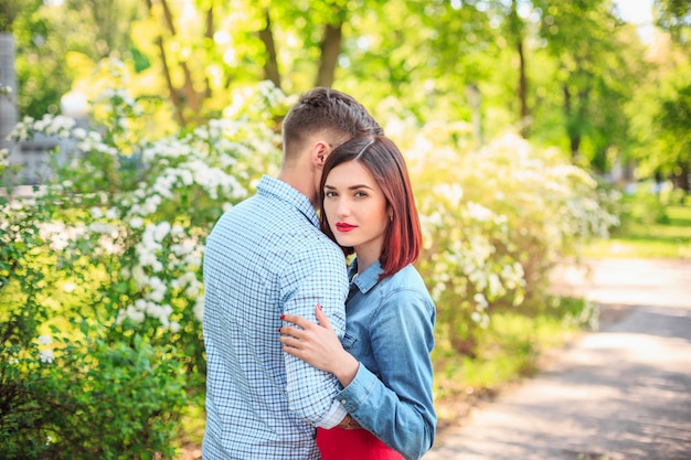 Feliz pareja joven en el parque de pie y riendo en el brillante día soleado