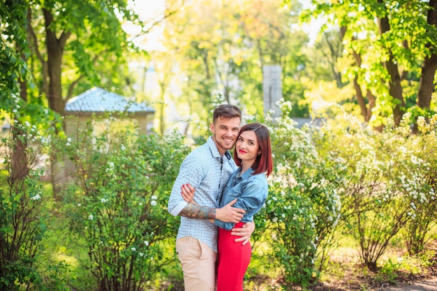 Feliz pareja joven en el parque de pie y riendo en el brillante día soleado