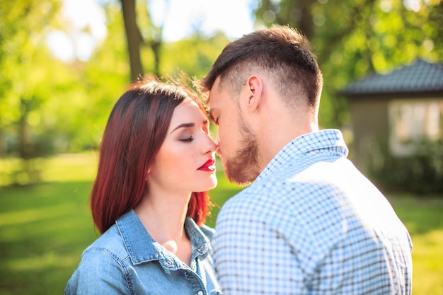 Feliz pareja joven en el parque de pie y riendo en el brillante día soleado