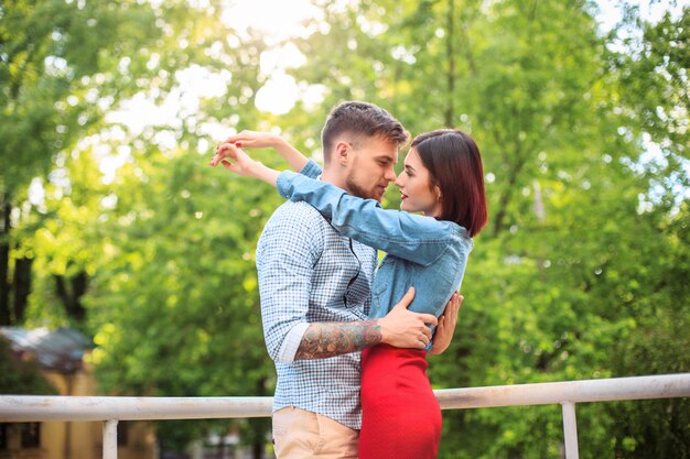 Feliz pareja joven en el parque de pie y riendo en el brillante día soleado