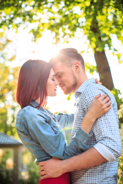 Feliz pareja joven en el parque de pie y riendo en el brillante día soleado