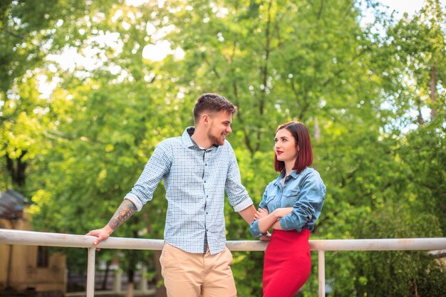 Feliz pareja joven en el parque de pie y riendo en el brillante día soleado