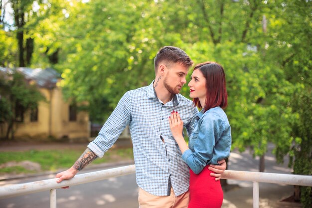 Feliz pareja joven en el parque de pie y riendo en el brillante día soleado