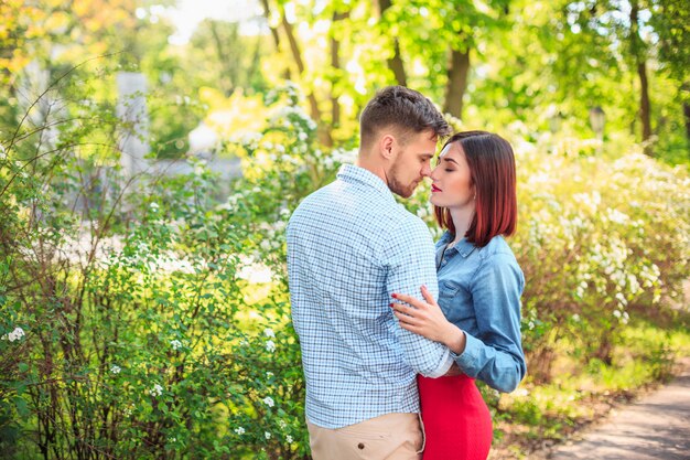 Feliz pareja joven en el parque de pie y riendo en el brillante día soleado