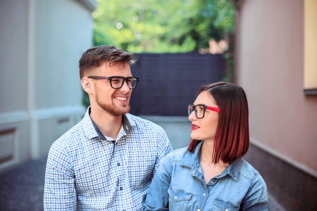 Feliz pareja joven de pie en la calle de la ciudad y riendo en el brillante día soleado