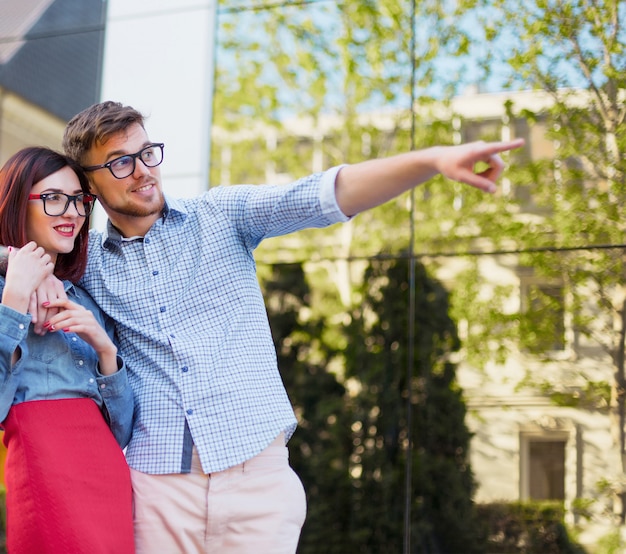 Feliz pareja joven de pie en la calle de la ciudad y riendo en el brillante día soleado