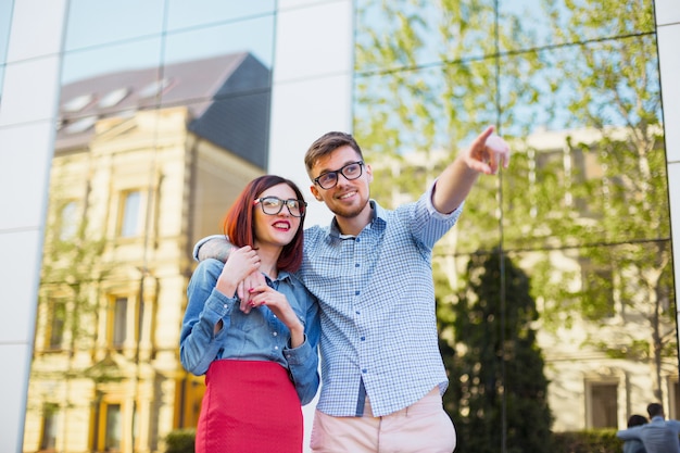 Feliz pareja joven de pie en la calle de la ciudad y riendo en el brillante día soleado