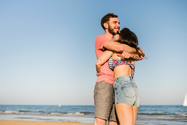 Foto gratuita feliz pareja joven romántica de pie frente al mar en la playa