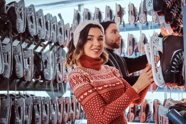 Foto gratuita una feliz pareja joven con ropa abrigada, eligiendo su talla en un vestuario, preparándose para patinar en la pista de hielo.