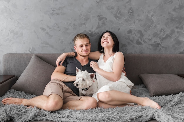 Feliz pareja joven sentada en el sofá con perro blanco