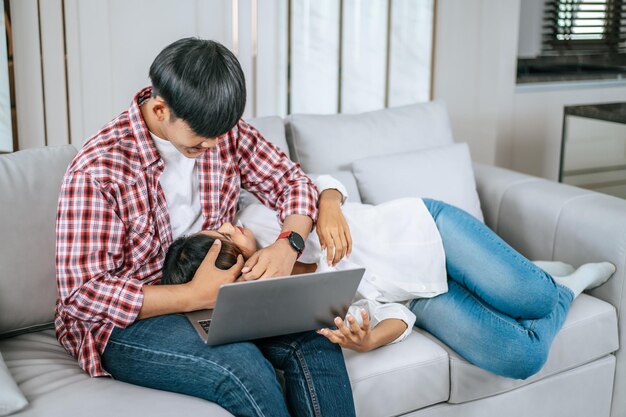 Feliz pareja joven sentada en un sofá en la sala de estar en casa usa una computadora portátil que trabaja hablando y sonríe junto con felicidad concepto de familia feliz