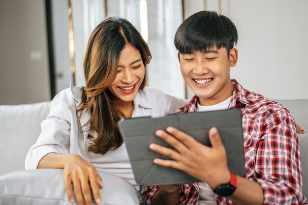 Feliz pareja joven sentada en un sofá en la sala de estar en casa usa una tableta con felicidad juntos concepto de familia feliz