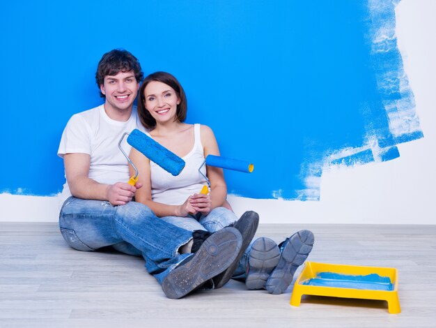 Feliz pareja joven siiting en el suelo cerca de la pared pintada