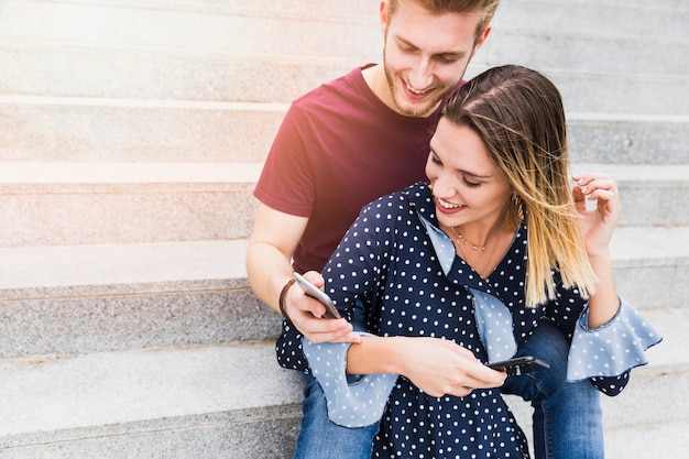 Feliz pareja joven con teléfono móvil sentado en la escalera