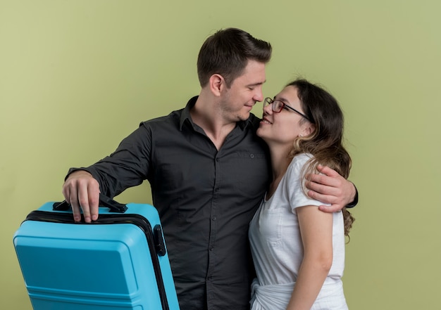 Foto gratuita feliz pareja joven de turistas hombre y mujer sosteniendo maleta mirando el uno al otro abrazándose sobre la luz