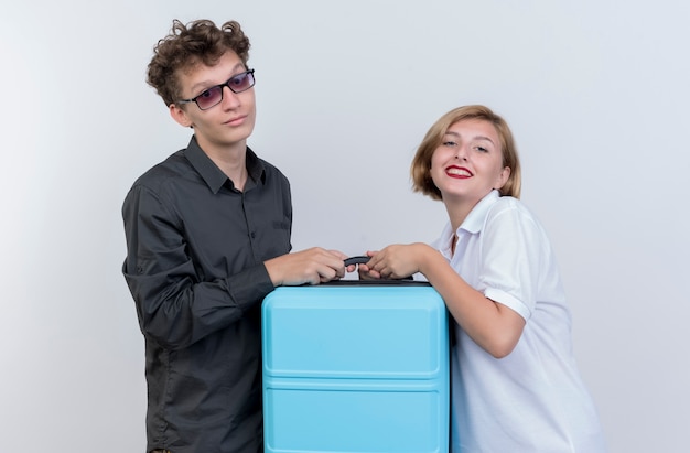 Feliz pareja joven de turistas hombre y mujer sosteniendo maleta sonriendo sobre pared blanca