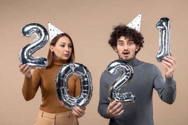 Feliz pareja joven usa sombrero de año nuevo posa para cámara Chica tomando y chico con y en gris