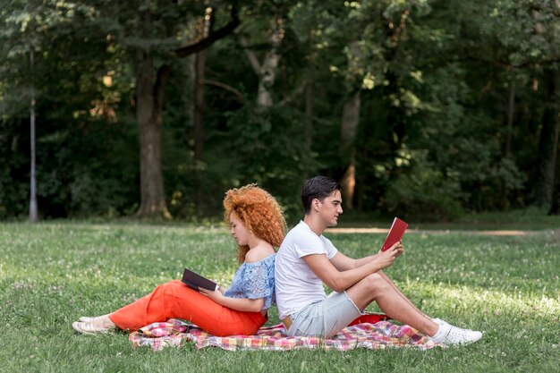 Feliz pareja de jóvenes sentados espalda con espalda en una manta de picnic